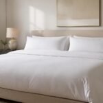 A wide king bed in a bright, calm bedroom, neatly made with crisp white cotton bed linen and the flat sheet folded back over the duvet in a clean band across the bed
